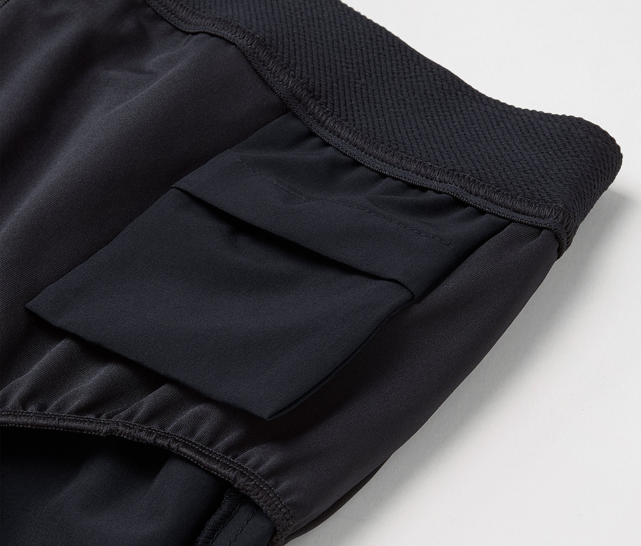 Detail einer schwarzen Sporthose mit Oberschenkeltasche und elastischem Bund.