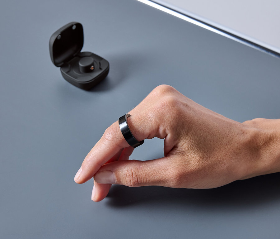 Eine Hand trägt einen schwarzen Ring. Neben dem Ring befindet sich eine offene Hülle.