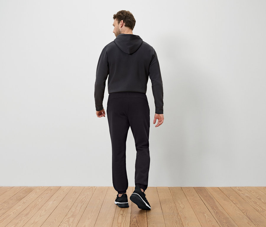 Mann von hinten trägt einen dunklen Kapuzenpullover und eine schwarze Trainingshose.