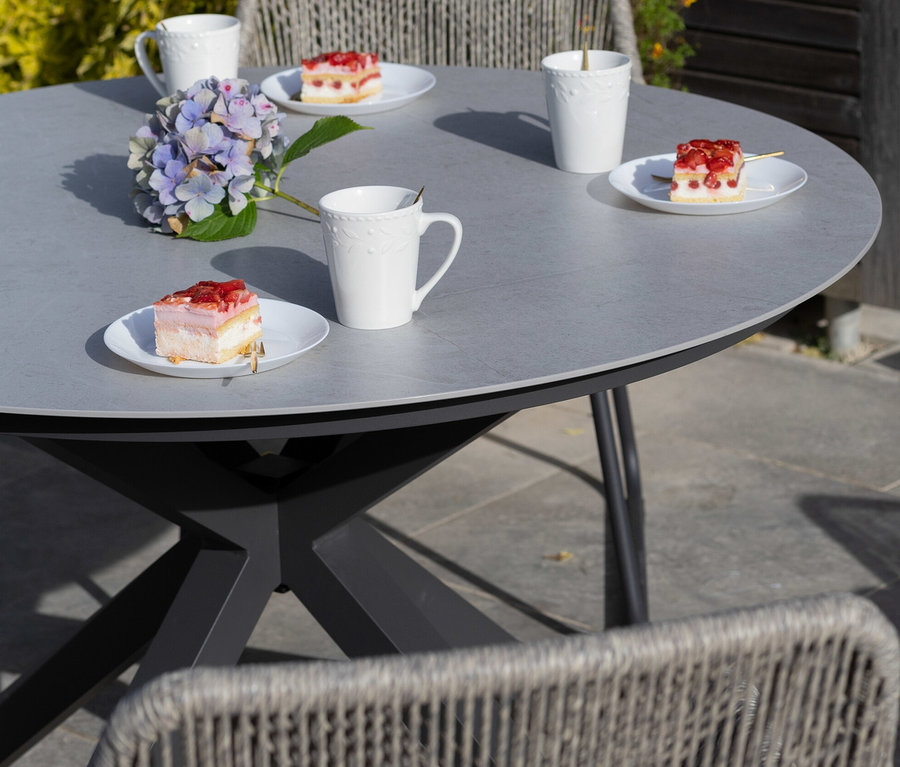 Grauer deVries Tisch mit ca. 120 cm Durchmesser mit Tassen und Kuchen.