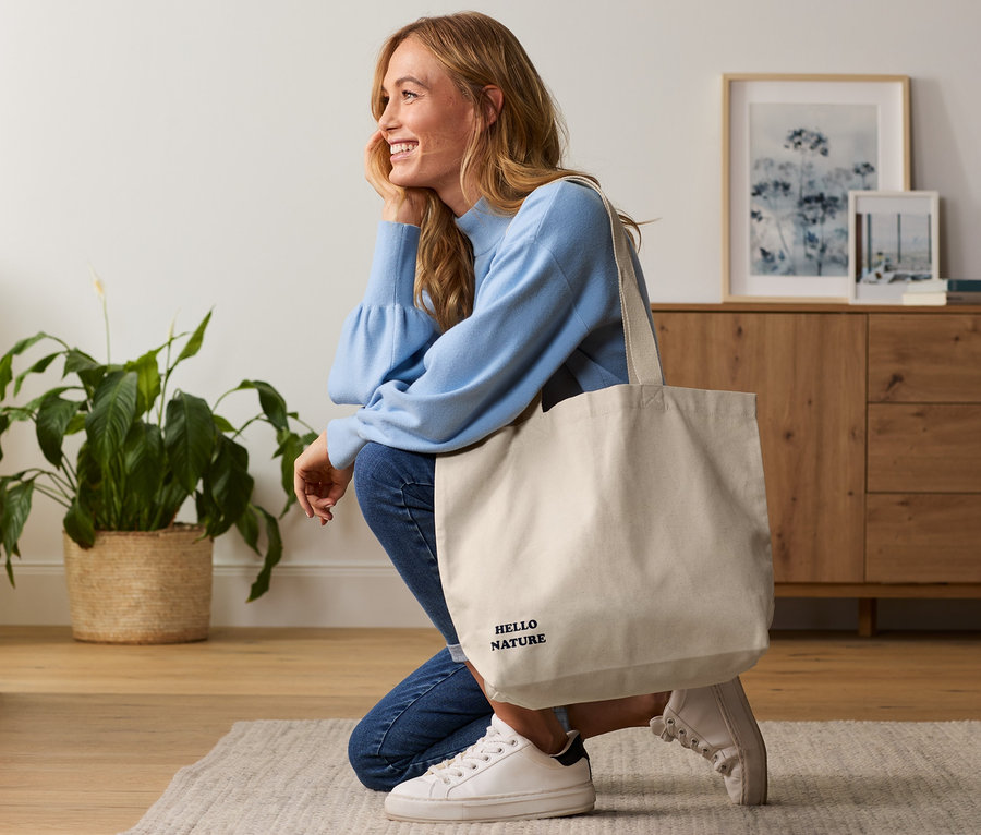 Frau kniet mit Canvas-Shopper mit dem Aufdruck Hello Nature.