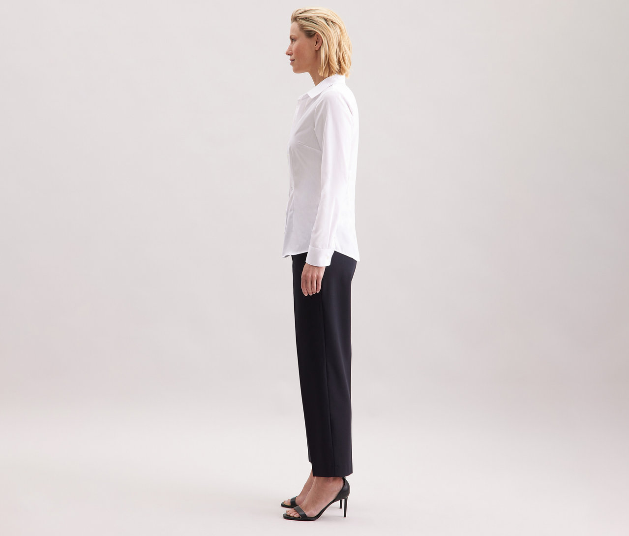 Frau im Profil, trägt eine weiße Seidensticker Bluse Slim Fit non iron, kombiniert mit einer dunklen Hose und schwarzen High Heels.