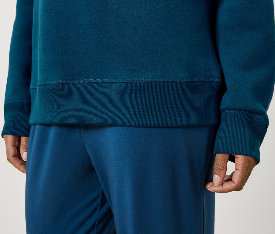 Person trägt ein blaugrünes Sweatshirt und blaue Trainingshose.