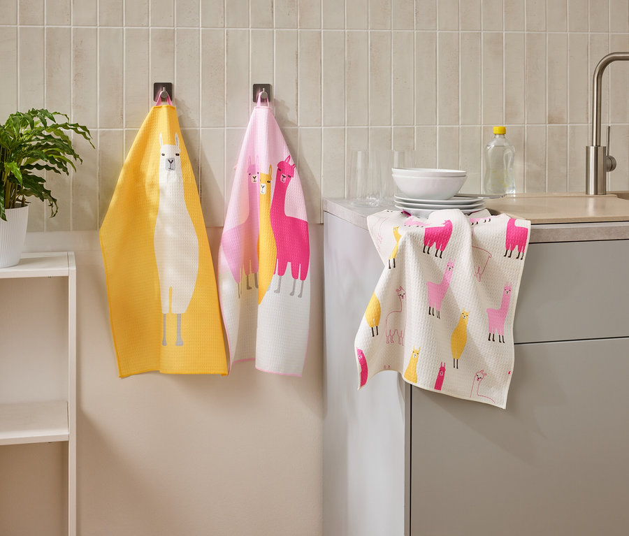 Drei Geschirrtücher mit Lama-Motiven hängen in einer Küche neben einem Waschbecken und einem Regal.