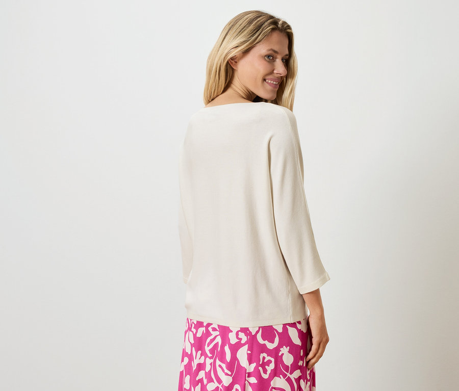 Blonde Frau mit beigem Oberteil und pinkem Rock mit Blumenmuster, Blick über die Schulter.