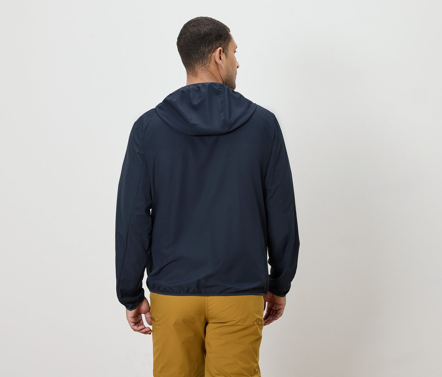 Ein Mann von hinten, der eine marineblaue Jacke mit Kapuze und gelbe Hosen trägt.