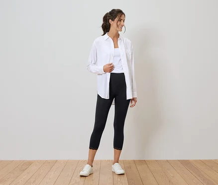 Frau mit weißem Hemd, Tanktop, schwarzen Leggings mit Spitze und weißen Turnschuhen.