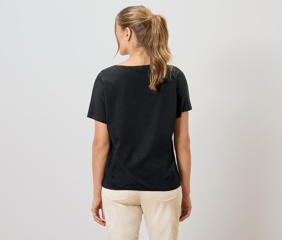 Frau von hinten, trägt ein schwarzes T-Shirt und helle Hosen.