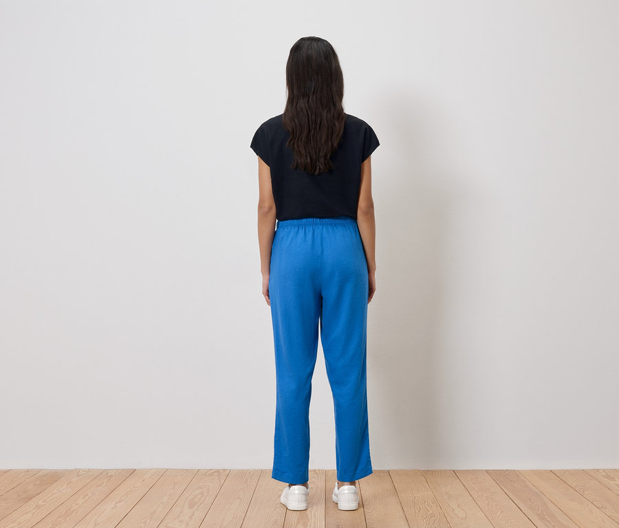 Rückansicht einer Frau mit dunklen Haaren, die ein schwarzes T-Shirt, eine blaue Hose und weiße Turnschuhe trägt.