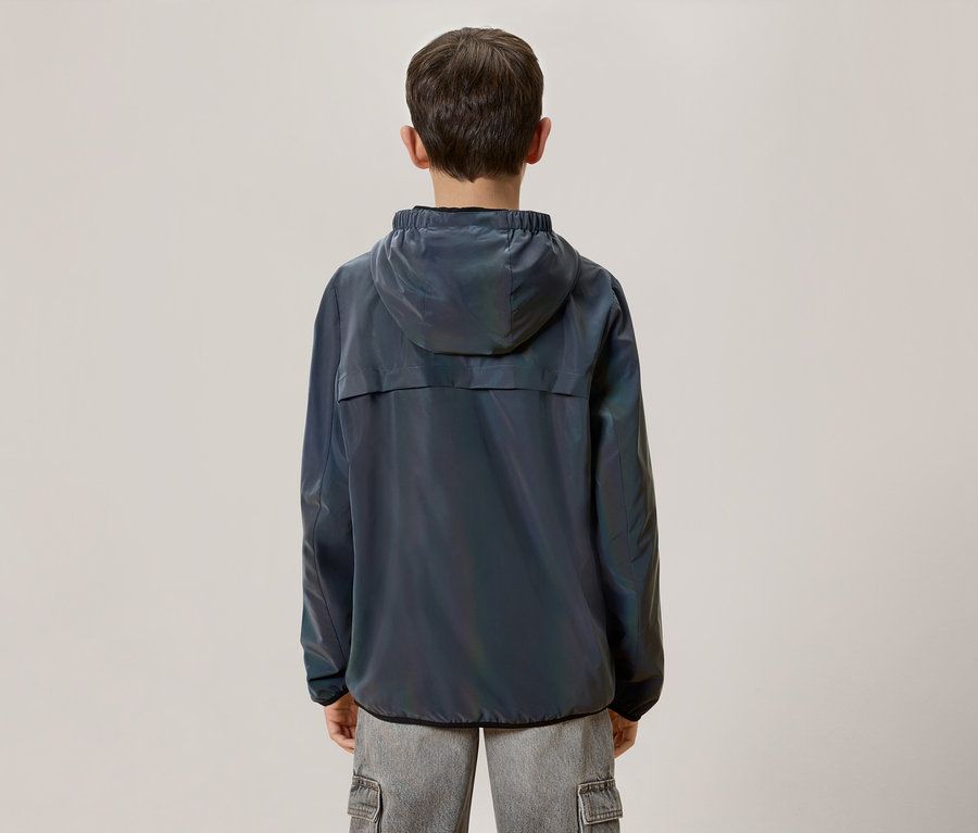 Rückansicht eines Jungen mit braunen Haaren in einer schimmernden, dunkelblauen Jacke mit Kapuze und grauen Cargohosen.