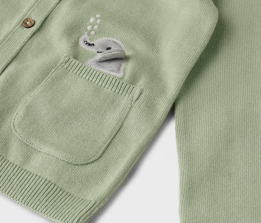 Nahaufnahme einer hellgrünen Strickjacke mit einer aufgestickten grauen Elefantenapplikation auf der Tasche und Holzknöpfen.