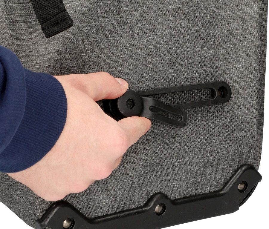 Nahaufnahme einer Hand, die eine schwarze Halterung an einer grauen Fischer Gepäckträgertasche Plus Cita befestigt.
