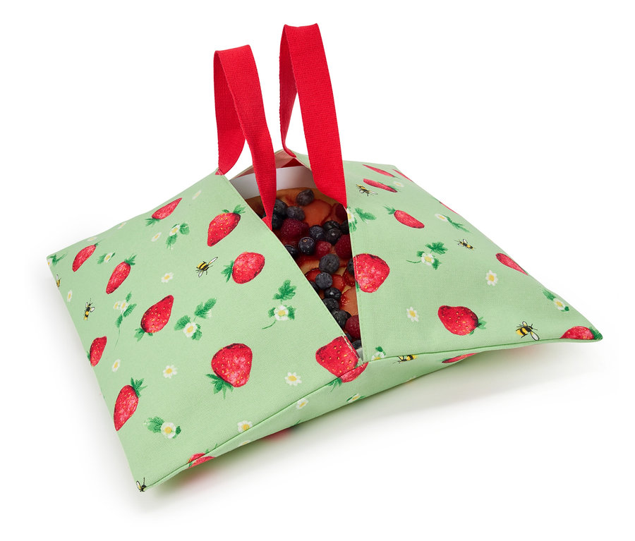 Erdbeerkuchen in einer grünen Stofftasche mit Erdbeermuster und roten Henkeln.