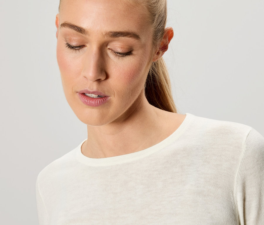 Porträt einer blonden Frau mit geschlossenen Augen, die ein cremefarbenes Langarmshirt trägt.