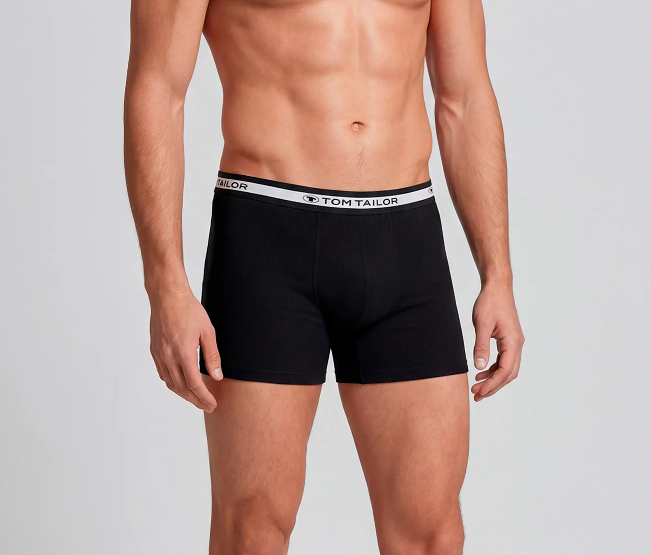 Oberkörper und Oberschenkel eines Mannes in schwarzen Boxershorts mit weißem Tom Tailor Bund.