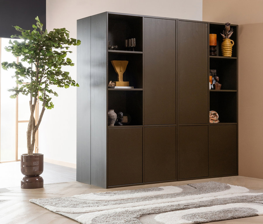 Dunkelbrauner modularer Schrank mit offenen Fächern und geschlossenen Türen, gefüllt mit Dekoartikeln. Links daneben steht eine große Topfpflanze. Davor liegt der WOOOD Teppich »Moro« in Grau und Weiß auf einem hellen Holzboden.