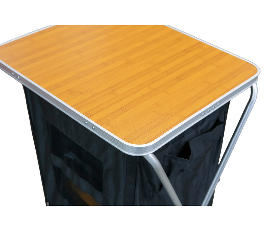 Nahaufnahme eines faltbaren Campingtisches mit Stauraum. Er hat eine hellbraune Tischplatte in Holzoptik und einen schwarzen Stoff-Stauraum darunter, mit silbernen Metallkanten.