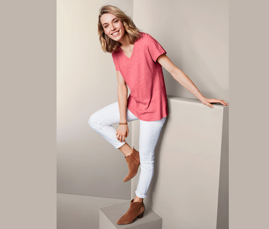Frau posiert in Leinenshirt, weißen Jeans und braunen Stiefeletten.