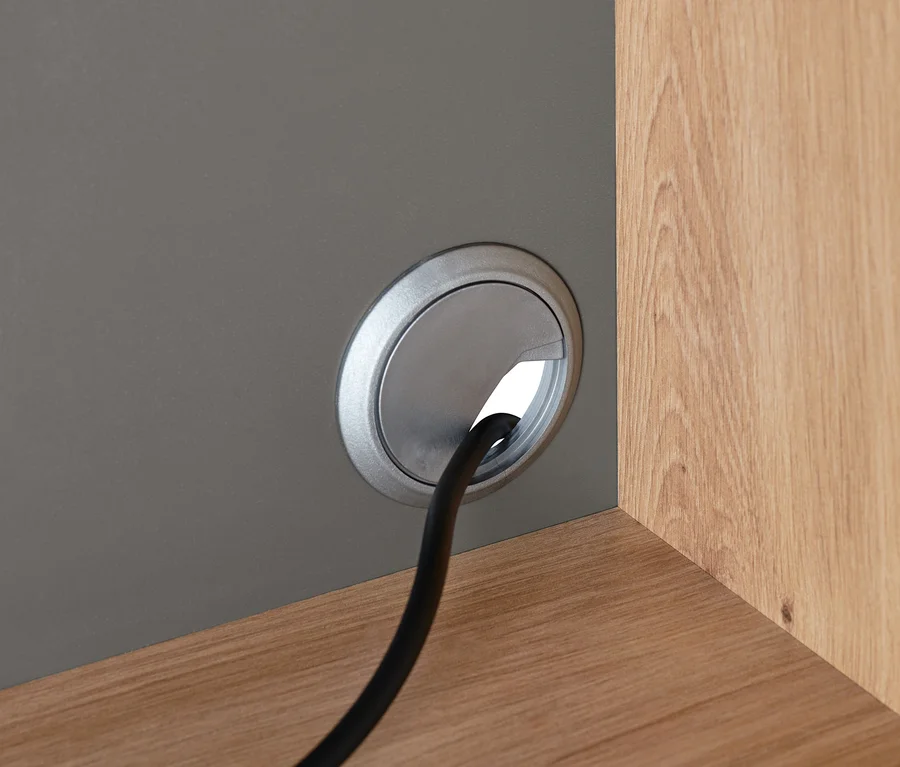 Detailansicht eines Büroschranks mit Arbeitsfläche, durch dessen Kabeldurchlass ein Kabel verläuft.