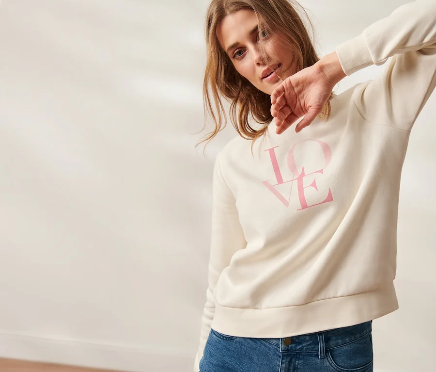 Frau posiert in einem cremefarbenen Sweatshirt mit dem Aufdruck LOVE.