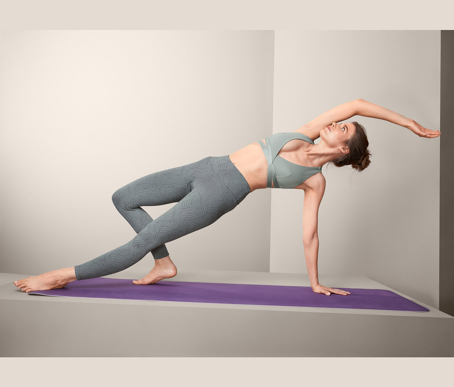 Frau macht Yogaübung auf lila Matte und trägt eine Bodyforming-Sporttight.