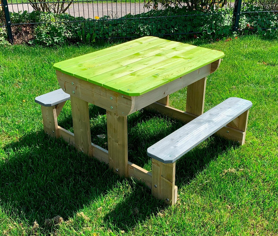 Ein grüner und grauer Wendi Picknick- und Matschtisch mit Bänken steht auf einer Wiese.