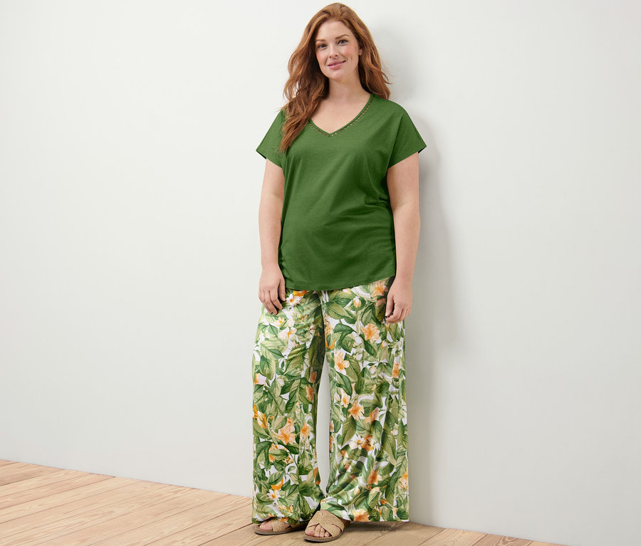 Frau steht und trägt ein grünes Shirt mit Crochet-Tape und eine bedruckte Palazzohose.