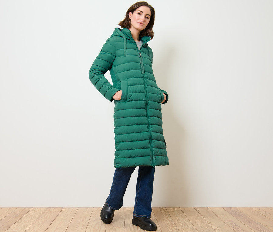 Frau posiert in langem Steppmantel mit Kapuze.