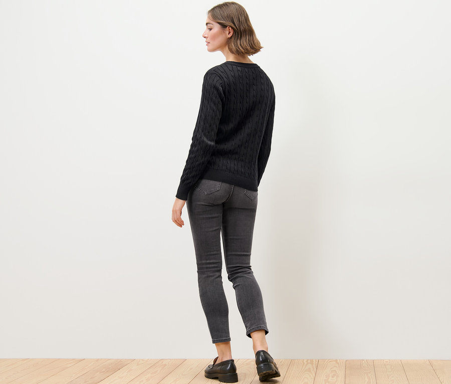 Frau trägt Feinstrickcardigan mit Zopfmuster, Jeans und Mokassins.