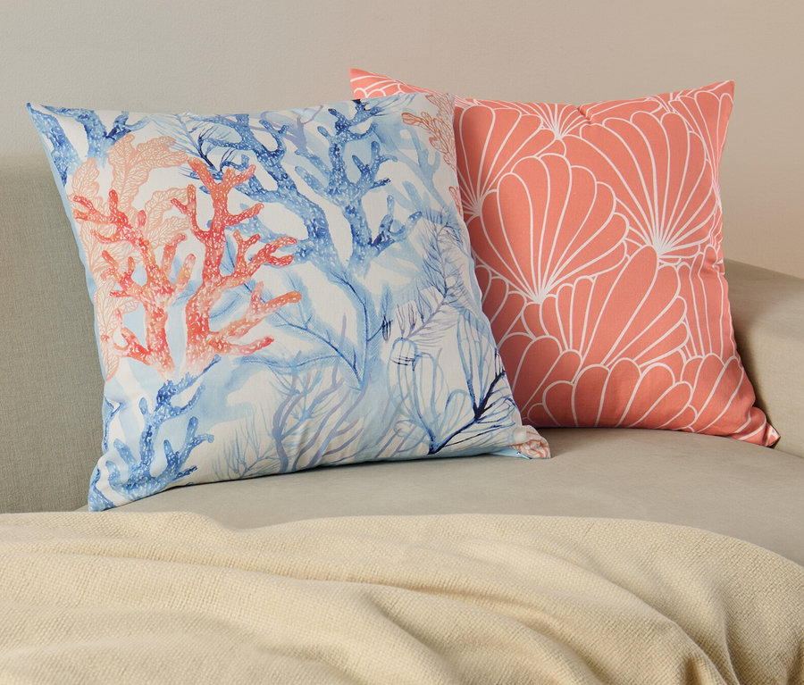 Zwei Dekokissen-Bezüge liegen auf einem Sofa. Einer mit Korallen- und blauem Muster, der andere mit einem Korallenblumenmuster.