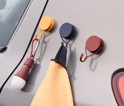 Drei Magnethaken sind an einem grauen Auto befestigt. An einem Haken hängt ein Handtuch, an dem anderen eine Lampe.