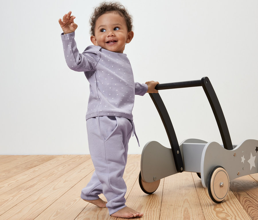 Ein Baby schiebt eine Lauflernhilfe und trägt eine gepunktete Baby-Sweathose.