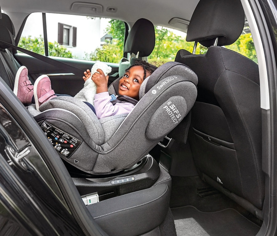 Ein lächelndes kleines Mädchen sitzt im Osann Kindersitz »Swift360 S« und hält ein Stofftier.