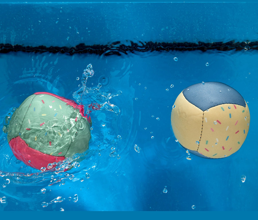 Zwei Wasserbälle im Wasser. Einer ist grün mit rosa Rändern und der andere ist gelb mit blauen Rändern.