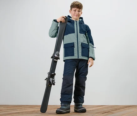Junge mit Kinder-Outdoor-und-Snowboardjacke hält Ski.