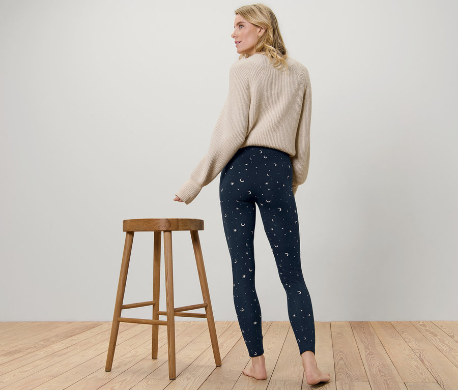 Frau steht mit dem Rücken zur Kamera und trägt eine kuschelige Leggings mit Stern- und Mondmuster.