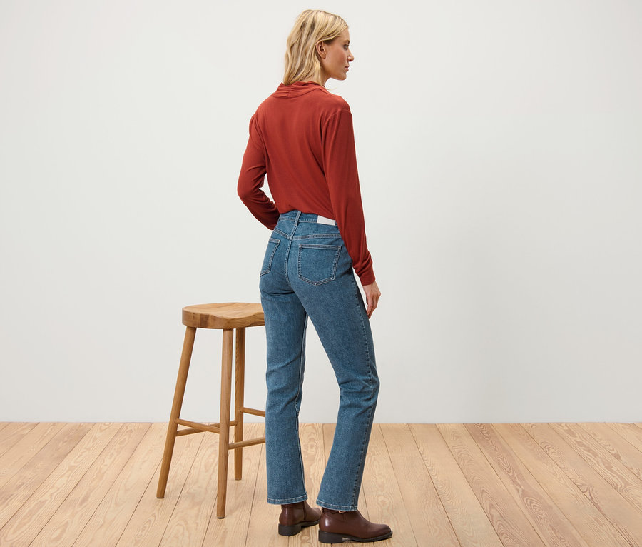 Frau steht seitlich und trägt eine Straight Jeans – Fit »Juna«, braune Stiefel und ein braunes Shirt.