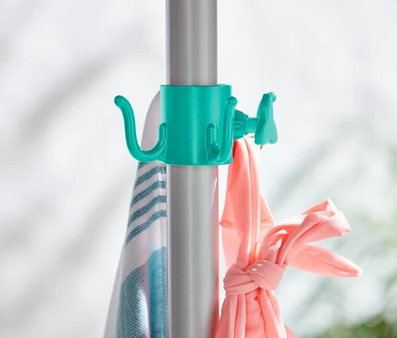 Zwei Sonnenschirm-Haken sind an einer silbernen Stange befestigt, an denen ein Handtuch und rosa Kleidung hängen.