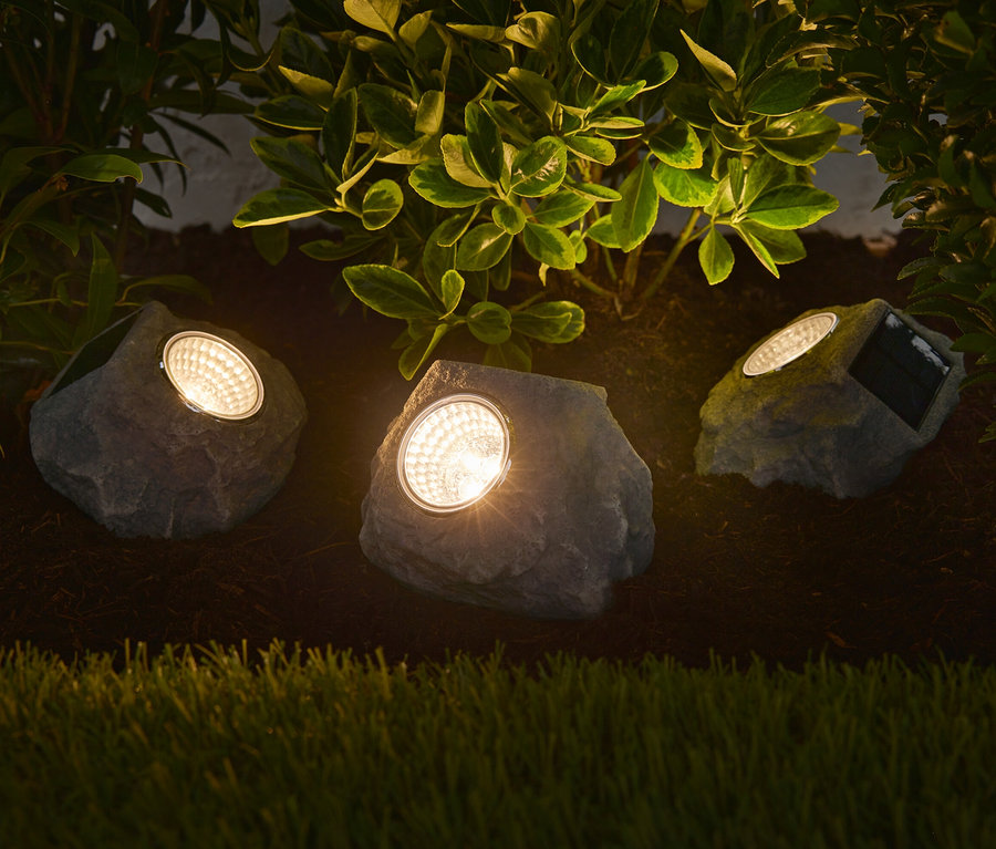 Drei Solar-LED-Steine beleuchten ein Blumenbeet.