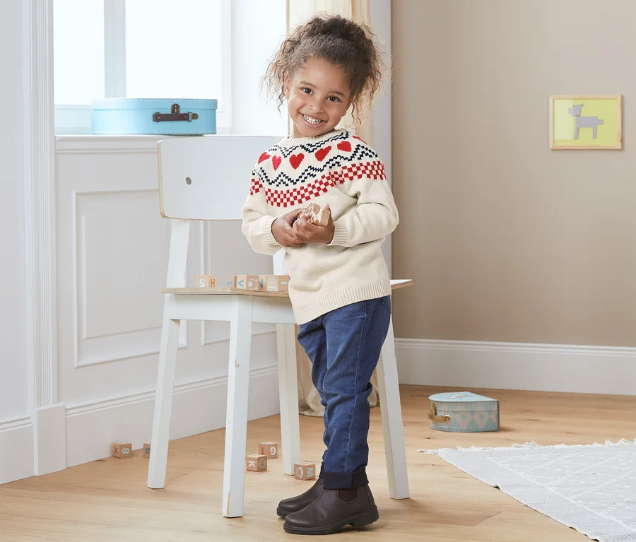 Mädchen steht in Norweger-Strickpullover und spielt mit Holzbausteinen.