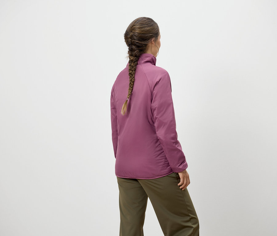 Frau mit Zopf steht mit dem Rücken zur Kamera und trägt eine rosafarbene Jacke und grüne Hosen.