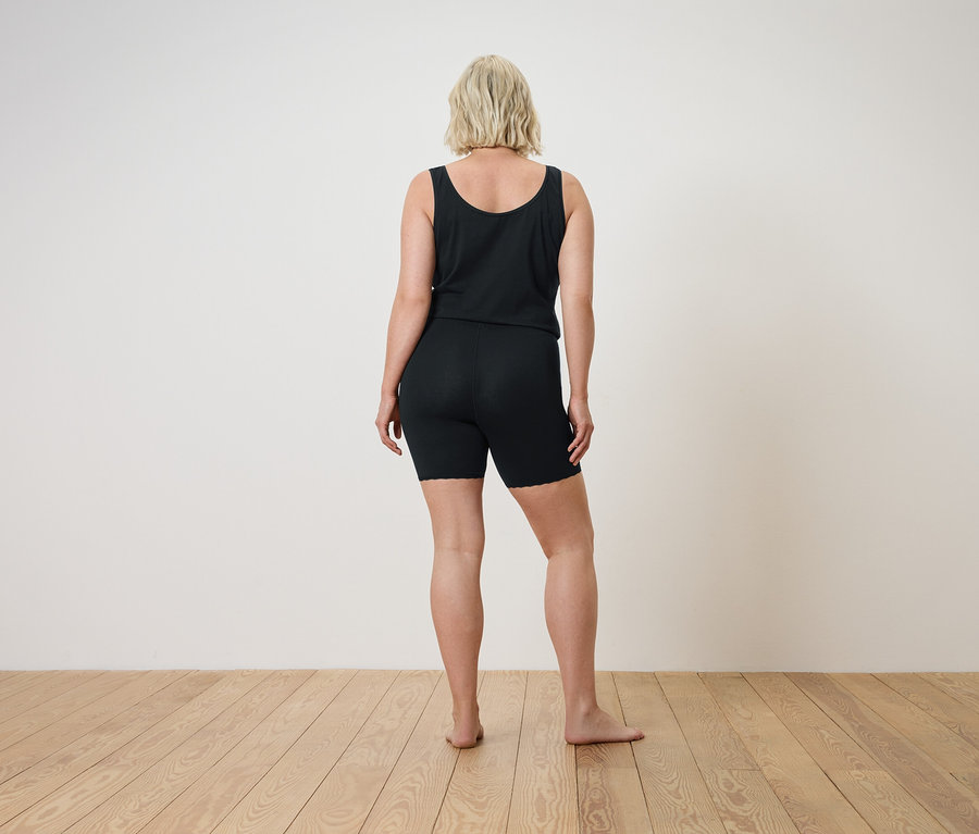 Rückansicht einer Frau mit blonden Haaren in schwarzem Tanktop und Shorts auf einem Holzboden.
