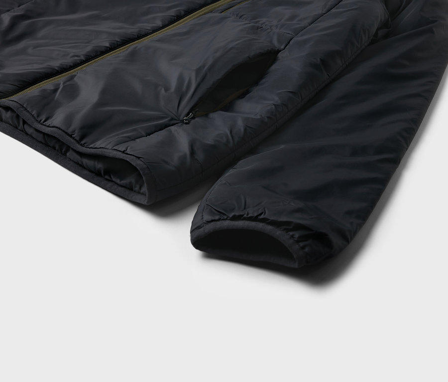 Detailaufnahme einer schwarzen Jacke mit Tasche und Ärmel auf hellem Hintergrund.