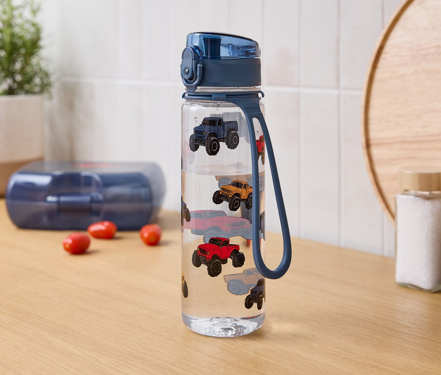 Auf einem Tisch stehen eine Wasserflasche mit Autoaufdruck, eine Lunchbox und Gewürzgläser.