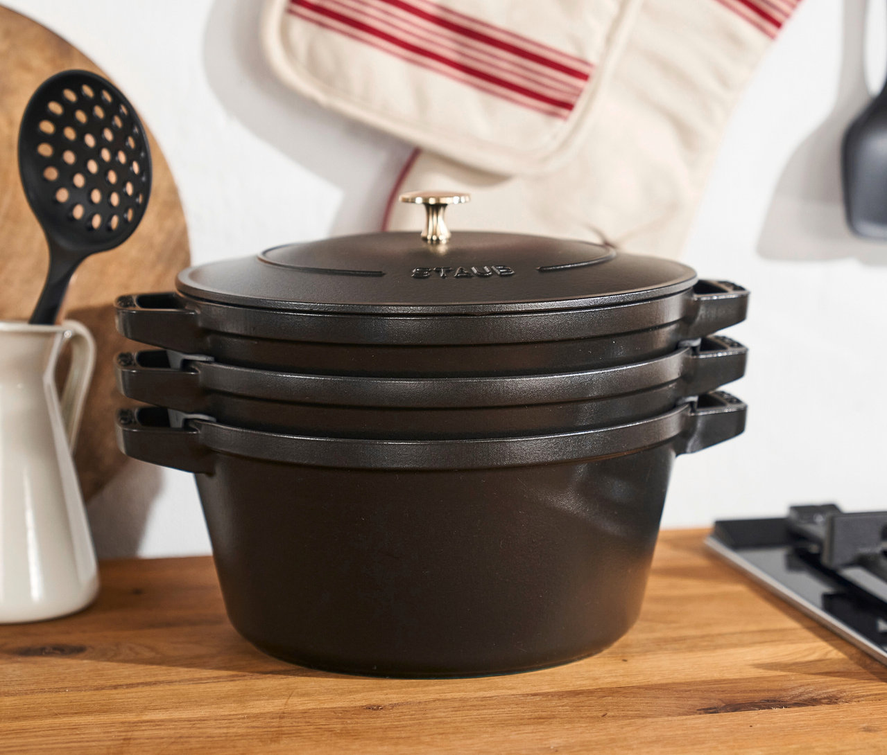 Drei schwarze STAUB Kochtöpfe »La Cocotte« aus einem 3-teiligen Set stehen gestapelt auf einer Küchentheke.