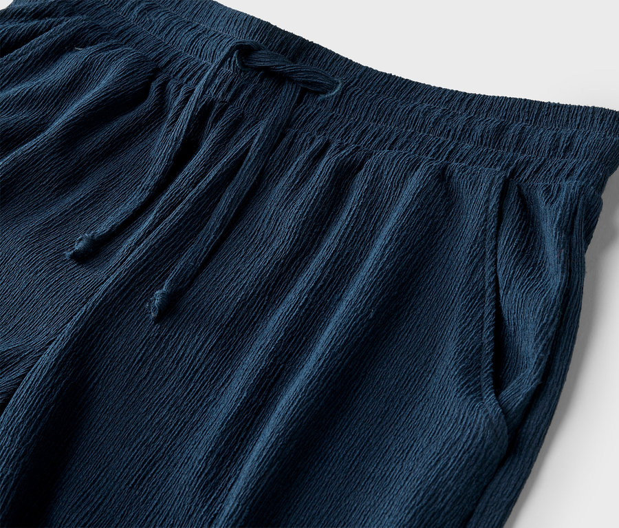 Nahaufnahme einer marineblauen Hose mit Kordelzug und Taschen vor einem weißen Hintergrund.