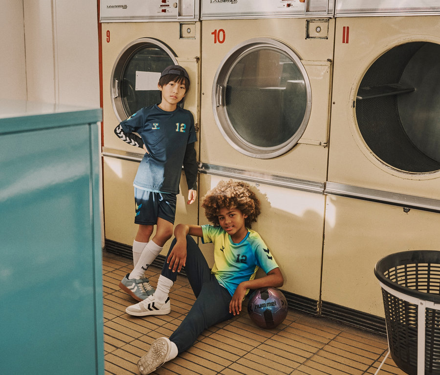 Zwei Jungen posieren in einem Waschsalon, einer steht und einer sitzt mit einem Fußball.