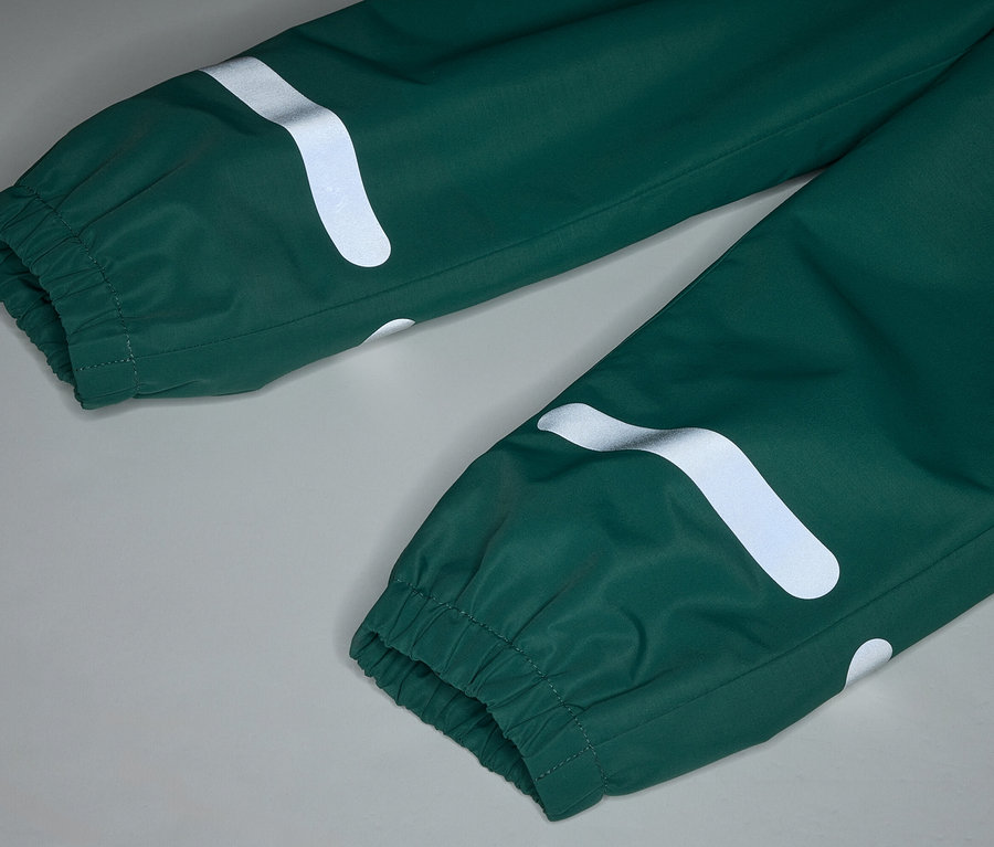 Nahaufnahme einer grünen Regenhose mit elastischen Bündchen und reflektierenden, gebogenen, weißen Streifen auf grauem Hintergrund.