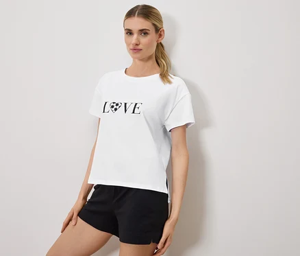 Frau trägt ein weißes T-Shirt mit dem Aufdruck "LOVE", wobei das O durch einen Fußball in Herzform ersetzt wurde, und schwarze Shorts.