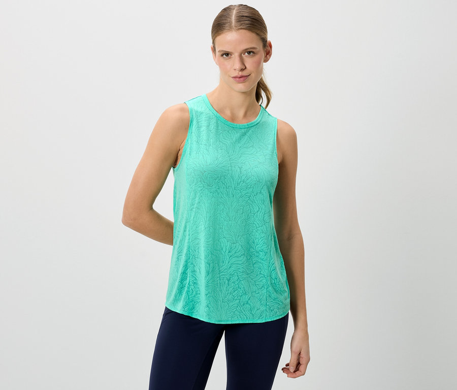 Frau trägt ein grünes Tanktop und blaue Leggings vor einem weißen Hintergrund.
